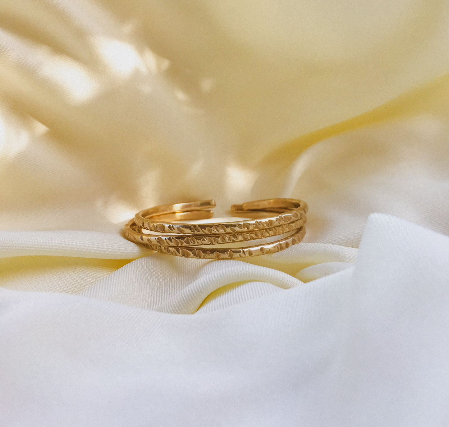A brass bracelet with intricate tad tad patterns, displayed on a white fabric surface.
