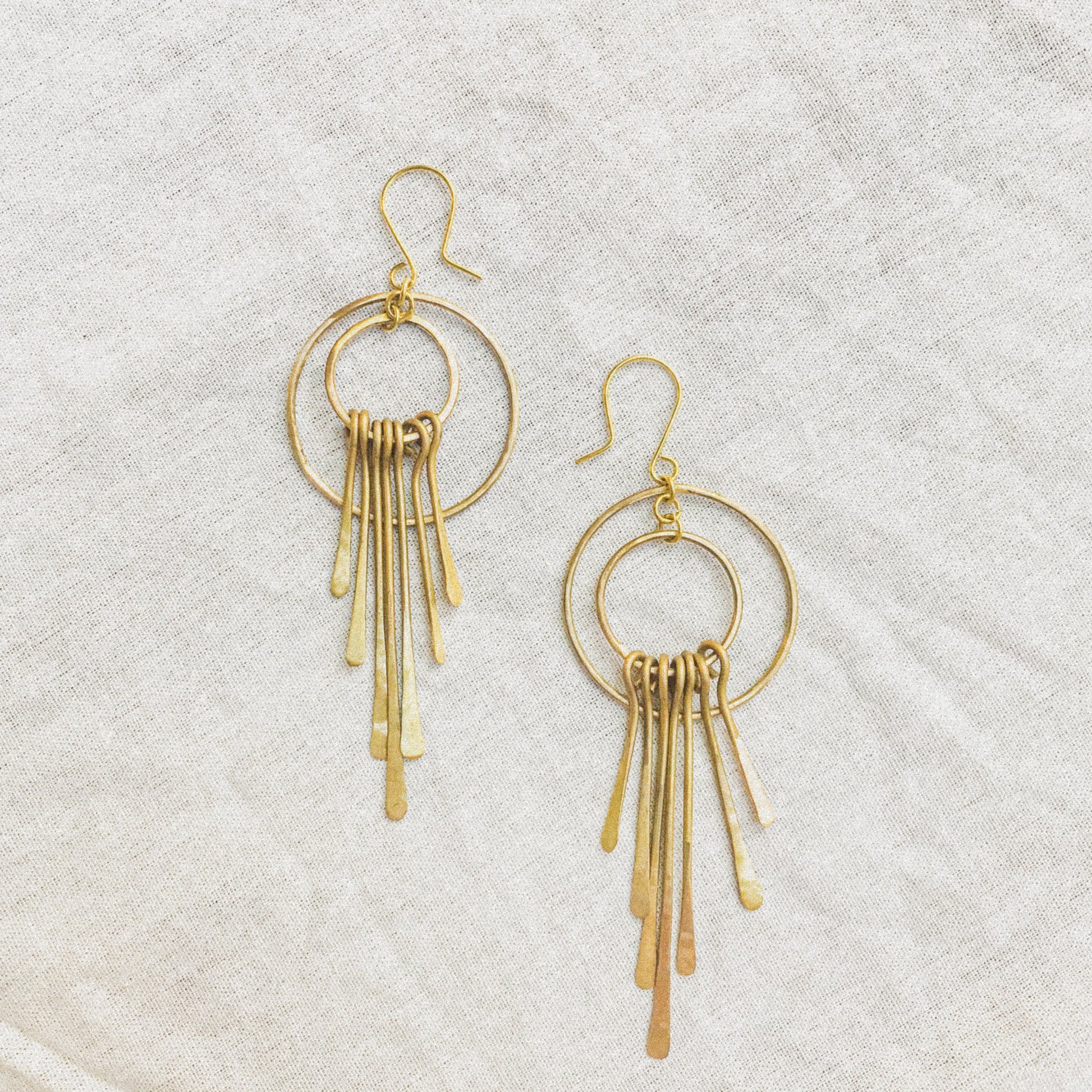 Gold hoop earrings with dangling elements on a light gray background