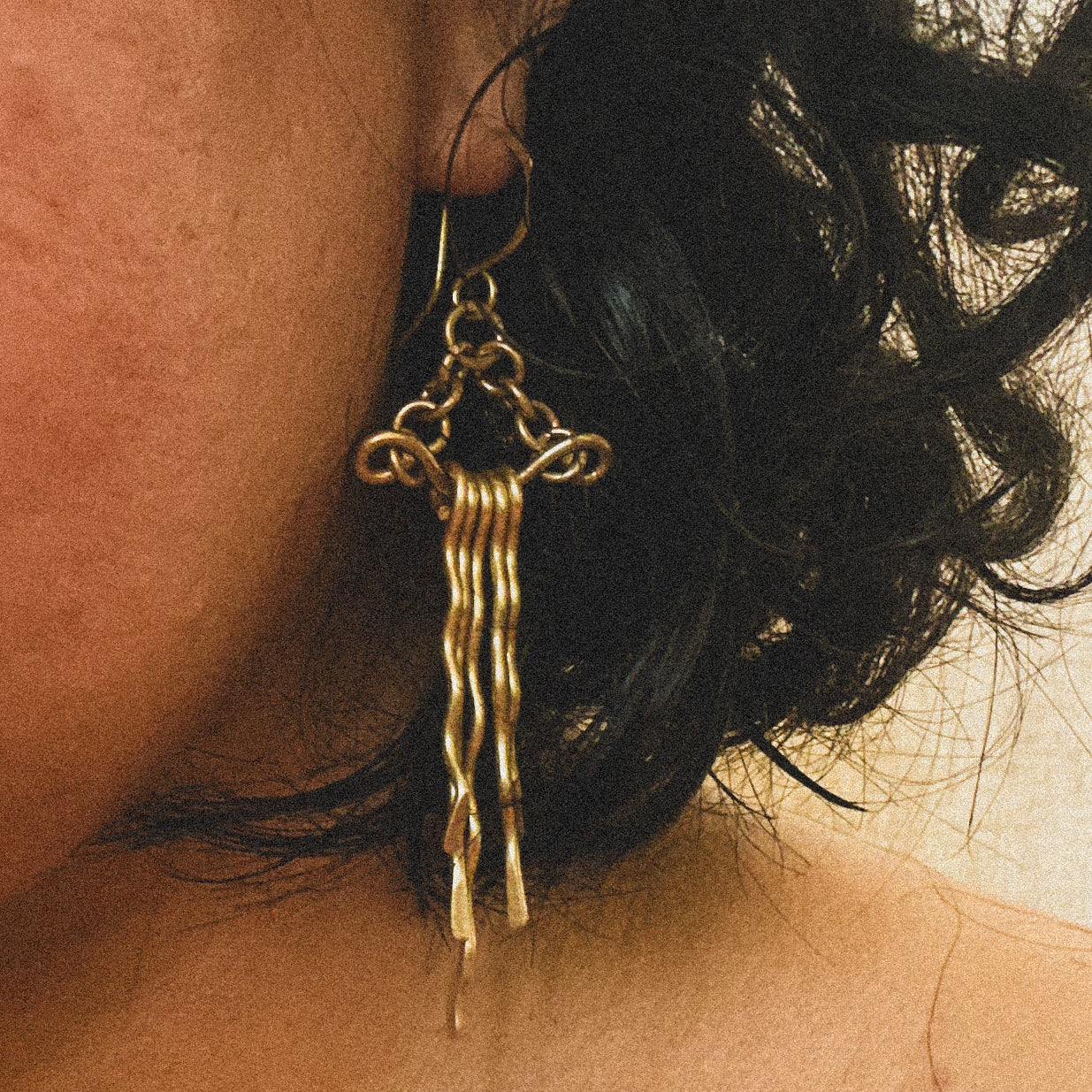 Close-up of a person wearing a gold earring with dangling strands.