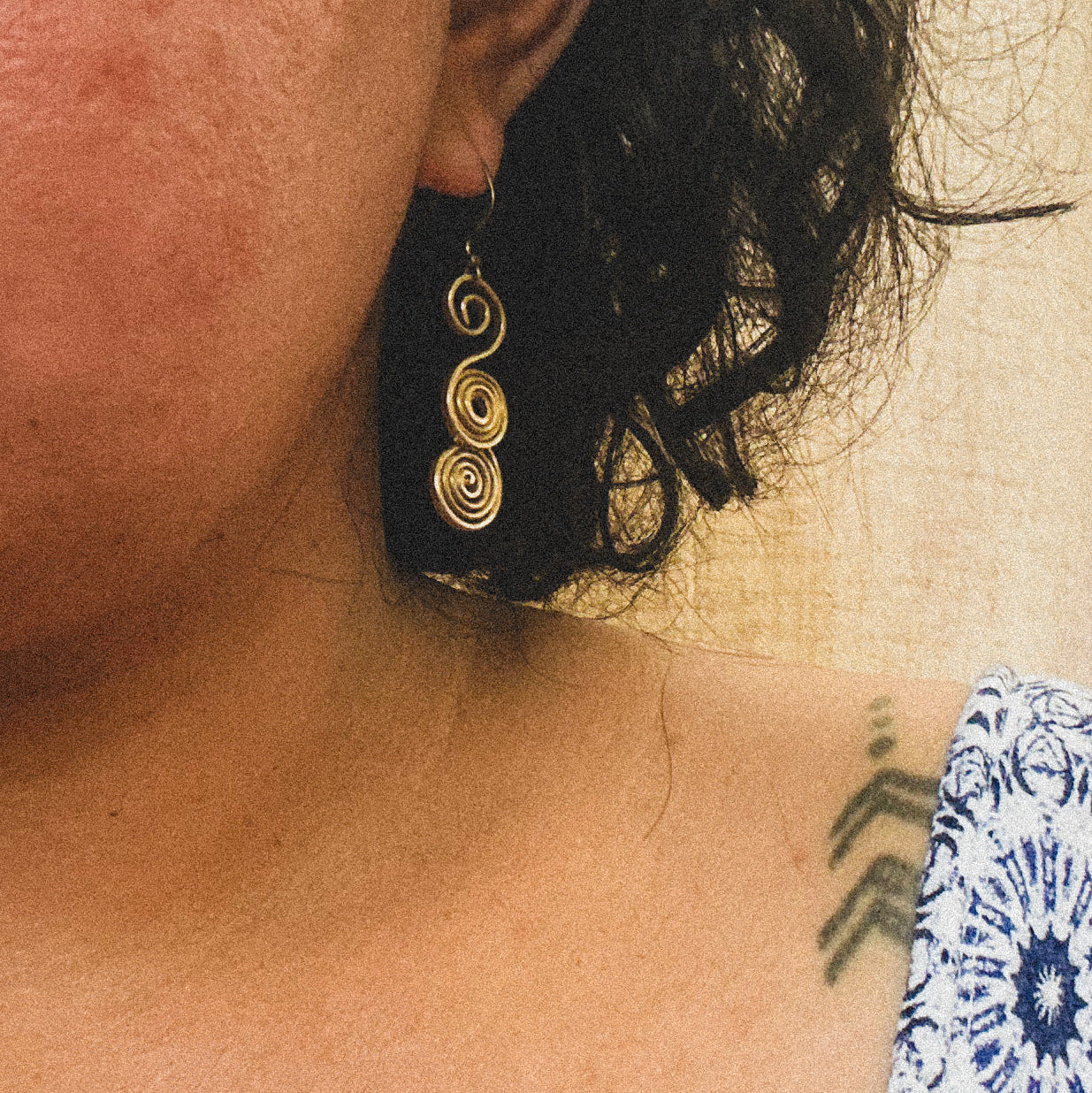 Close-up of an ear wearing a gold spiral earring with a blurred background