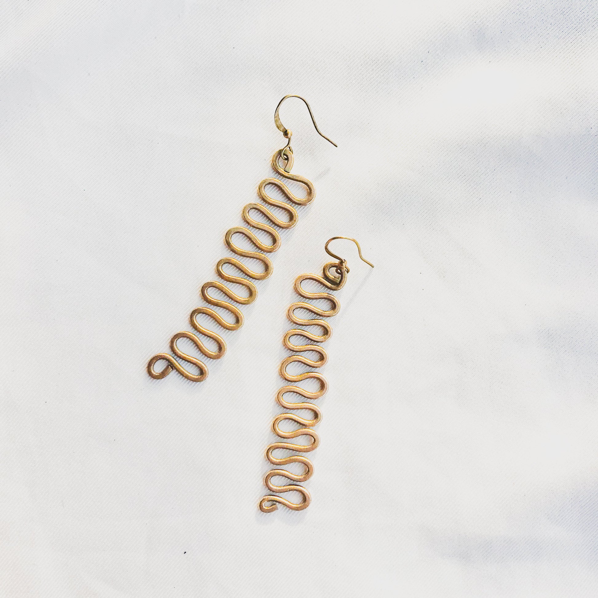 Gold wavy earrings on a light gray background